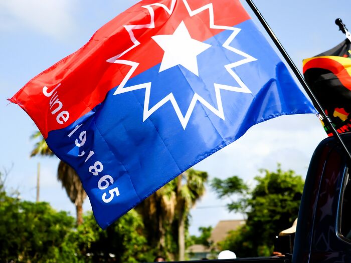 A Juneteenth flag, red and blue with a white star and the date June 19, 1865, waving in the wind, a hard to forget fact.