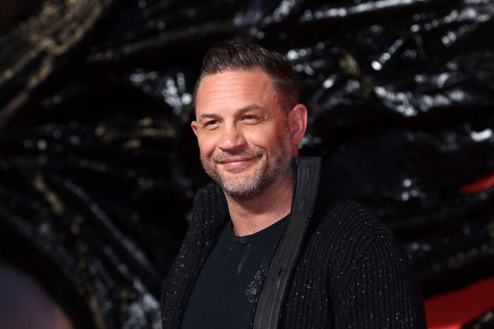 Actor Tom Hardy smiling at an event with dark background