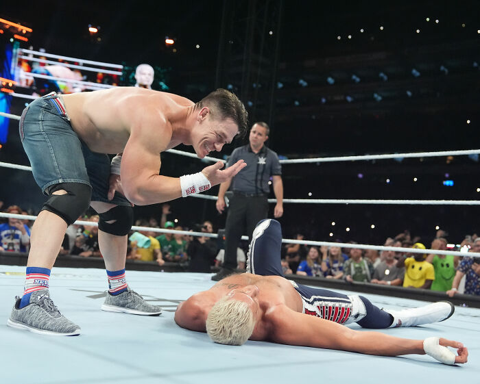 John Cena in the wrestling ring, looking at a fallen opponent, before his hair transplant reveal.