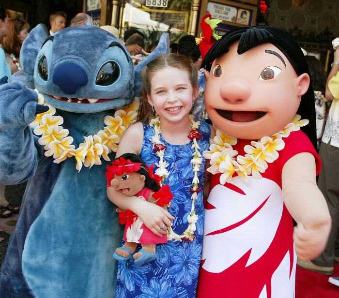 Young actress Daveigh Chase posing with Lilo & Stitch characters, wearing a blue floral dress and flower leis. Young actress Daveigh Chase posing with Lilo & Stitch characters, wearing a blue floral dress and flower leis.