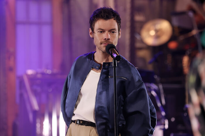 A man singing into a microphone, wearing a blue jacket and white shirt. Olivia Wilde, Don't Worry Darling.