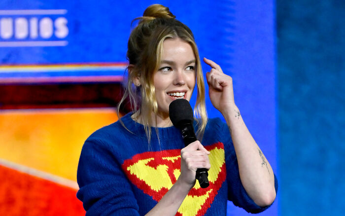 Supergirl star speaking on stage wearing superhero sweater