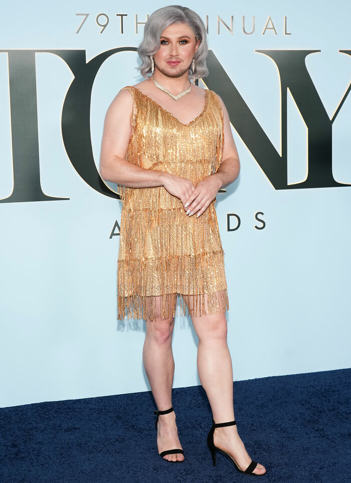 Person in gold fringe dress posing at Tony Awards event