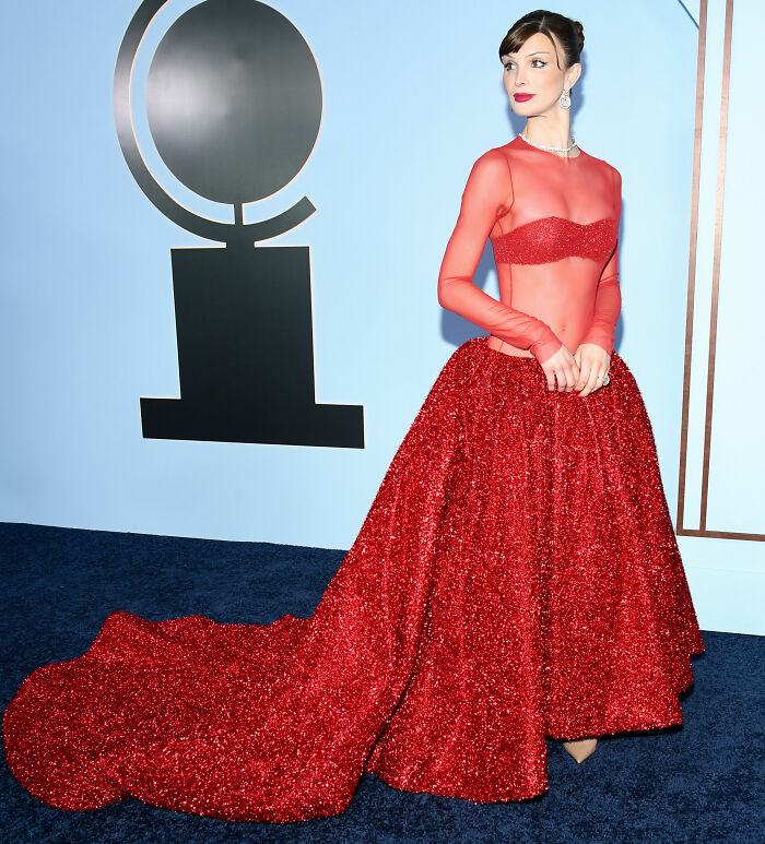 Woman in a sparkling red gown with sheer top and long train at the Tony Awards