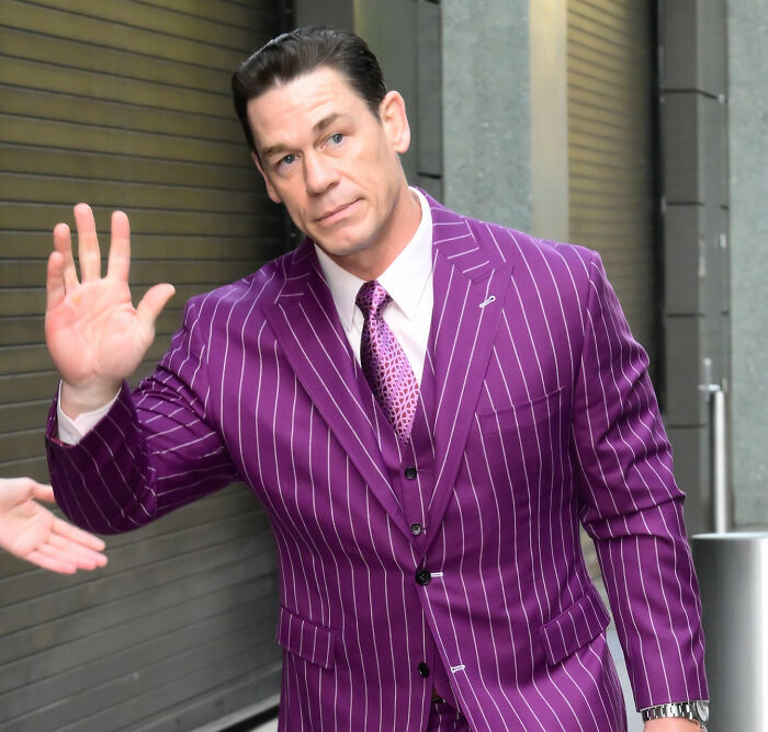 John Cena with new hair, waving in a purple pinstripe suit after a hair transplant.