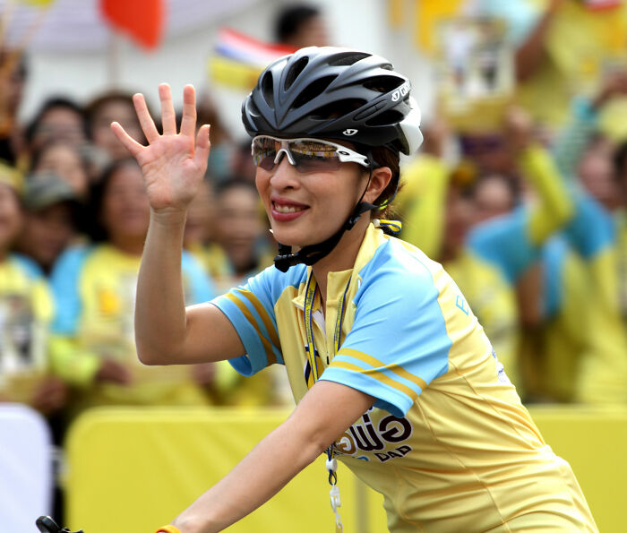 Thai princess waving while cycling, wearing helmet and yellow-blue jersey at public event Thai princess waving while cycling, wearing helmet and yellow-blue jersey at public event