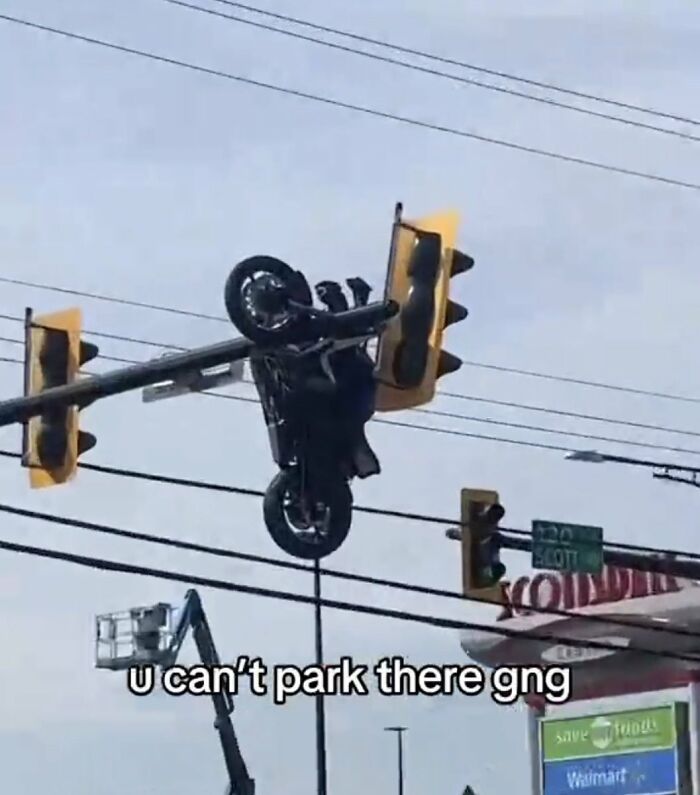 A motorcycle hanging upside down from a traffic light pole, a cringe image.