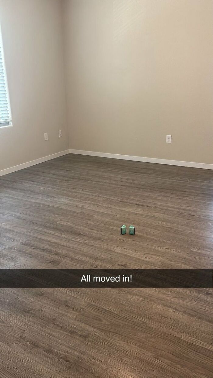 Minimalist cringe image of an empty room with only two small bottles on the floor, captioned All moved in!