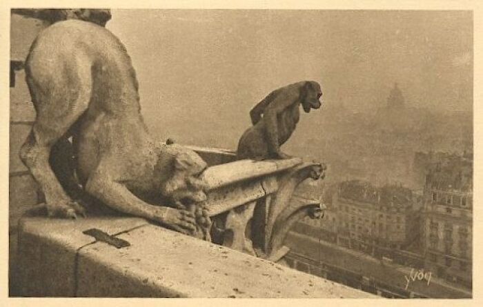 A sepia-toned image of gargoyles still intact, overlooking a distant city on a hazy day. The interesting objects highlight impressive preservation.