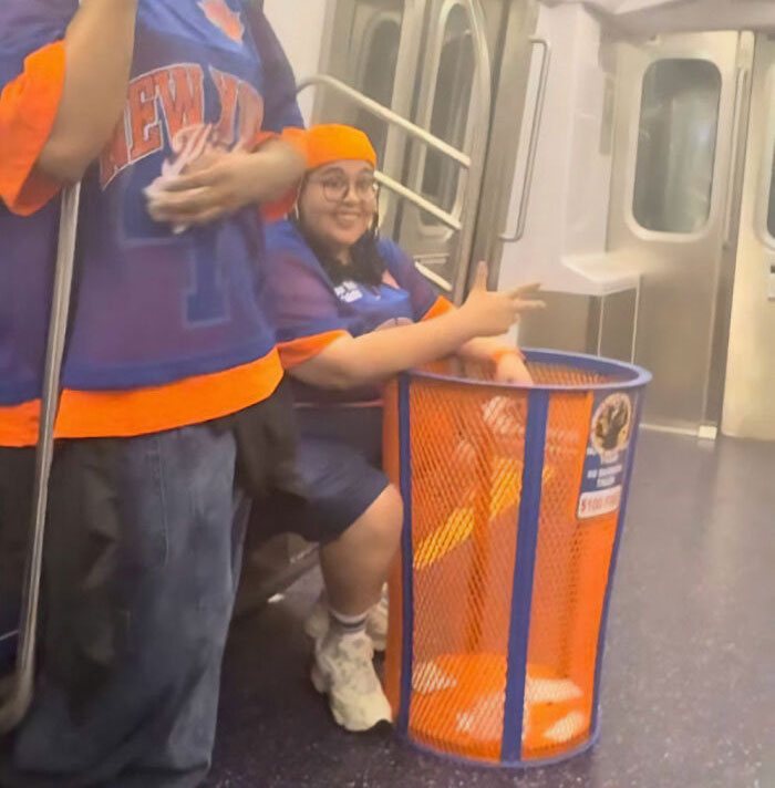 A person in a Knicks jersey with a stolen Knicks trashcan on a subway train, following the JPMorgan exec viral video.