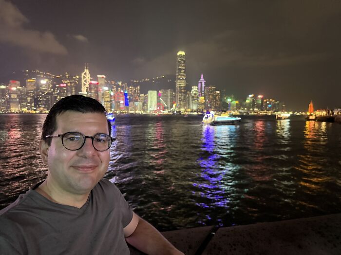A traveler smiling with the stunning Hong Kong skyline and harbor in China at night, a vibrant travel experience.