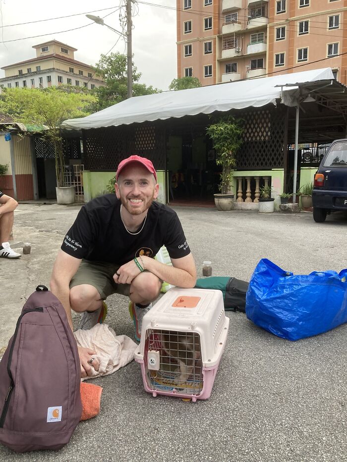 A man smiling and crouching next to a cat carrier, having helped street cats with local action and technology.