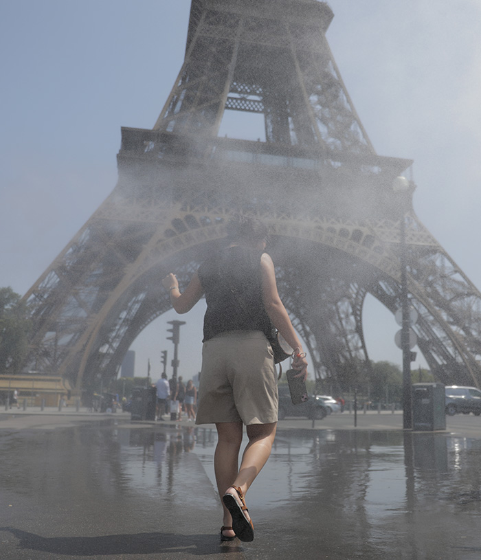 A person walks through mist in front of the Eiffel Tower, experiencing Paris heat wave and climate crisis. A person walks through mist in front of the Eiffel Tower, experiencing Paris heat wave and climate crisis.