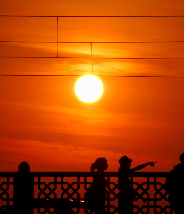 Silhouettes of people against a vibrant orange sunset, symbolizing the intense heat wave and climate crisis. Silhouettes of people against a vibrant orange sunset, symbolizing the intense heat wave and climate crisis.