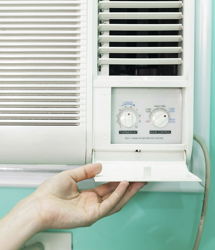 A hand adjusting a thermostat on a window air conditioning unit, suggesting a need for cooling during a heat wave and climate crisis. A hand adjusting a thermostat on a window air conditioning unit, suggesting a need for cooling during a heat wave and climate crisis.