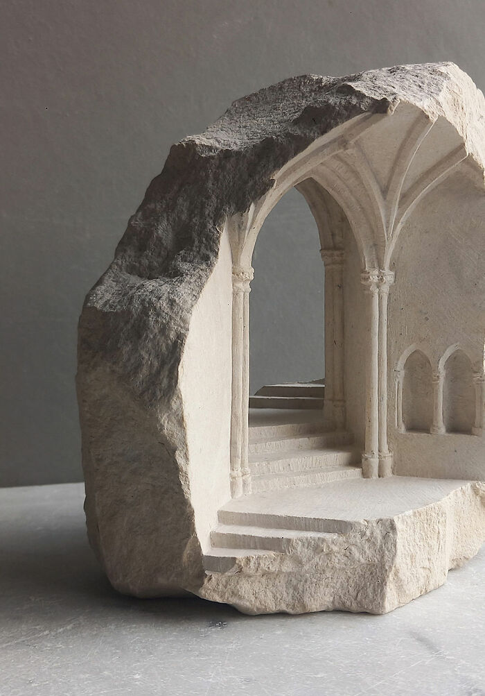 Artist carves tiny architectural models of ancient buildings with a grand archway and staircase into solid stone.