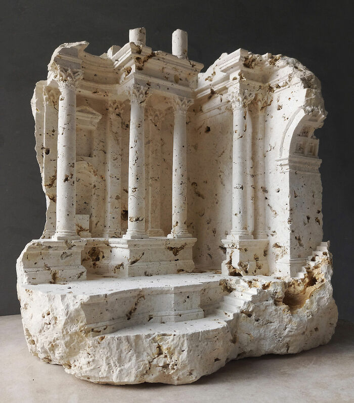Artist carves tiny architectural models of classical buildings, featuring detailed columns and steps, into solid stone.