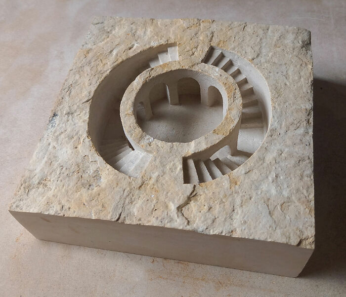Artist carves tiny architectural model of a classical building in solid stone, with a detailed spiral staircase.