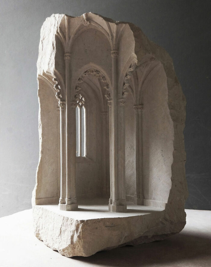 Artist carves tiny architectural model of an ancient building in solid stone, showcasing intricate gothic arches.
