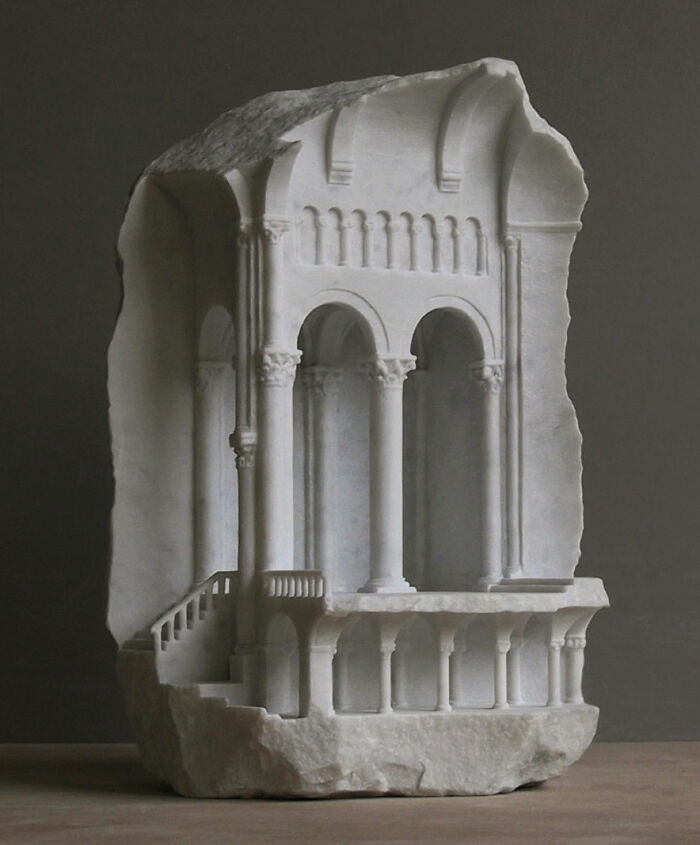 Artist carves tiny architectural models of ancient buildings into solid stone, depicting a multi-story structure with columns.