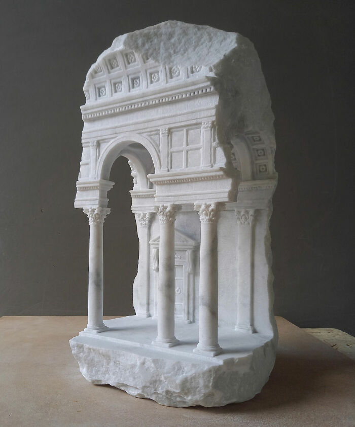 Artist carves tiny architectural models of classical buildings into solid stone, featuring an intricate arched entrance.
