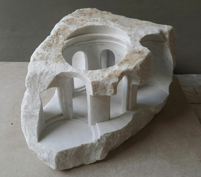 Artist carves tiny architectural model of an ancient building in solid stone, showing a circular structure.