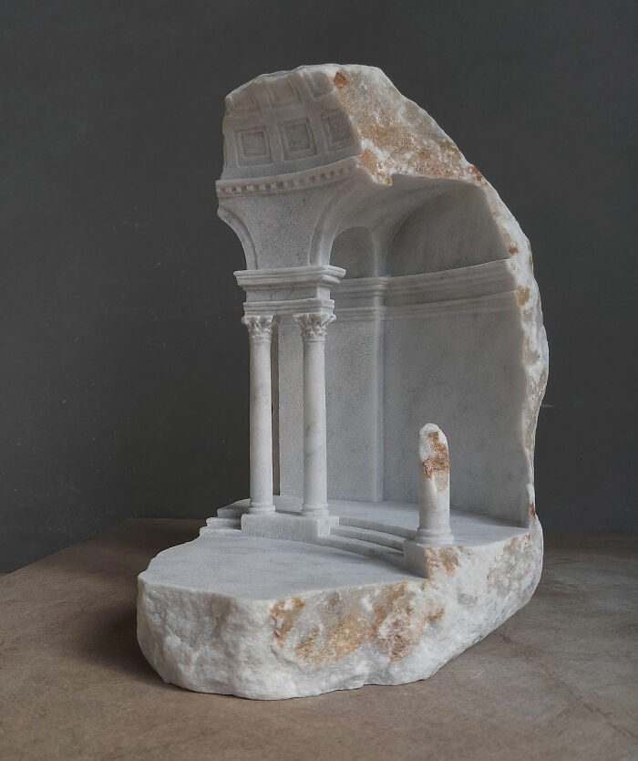 Artist carves tiny architectural models of ancient buildings into solid stone, showing a detailed facade with columns.