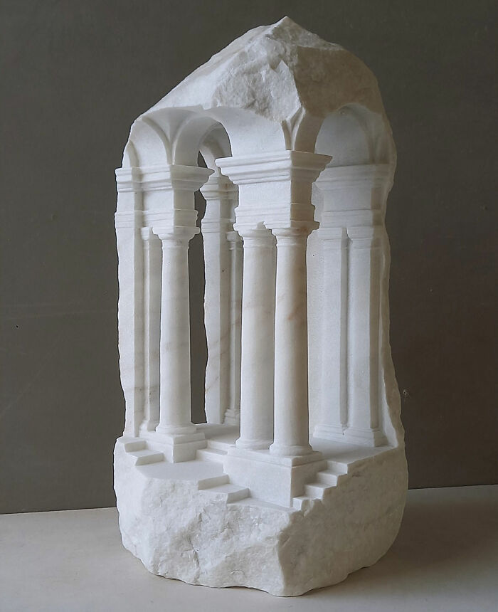 Artist carves tiny architectural models of ancient buildings into solid stone, featuring intricate columns and arches.