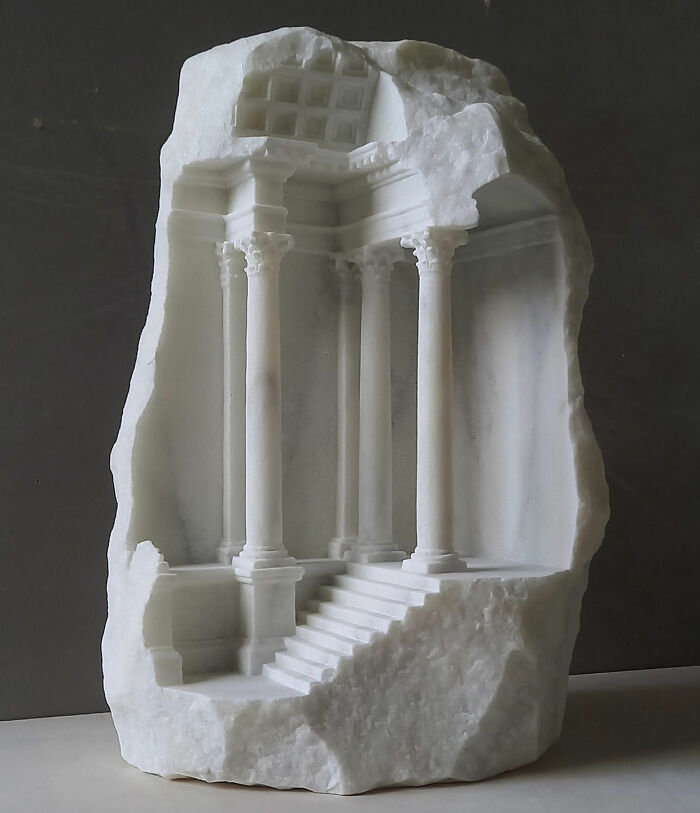 Artist carves a tiny architectural model of an elaborate classical building with columns and stairs into solid stone.