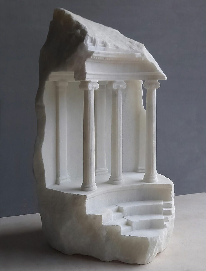 Artist carves tiny architectural models of ancient buildings into solid stone, showcasing a classical temple facade with columns.