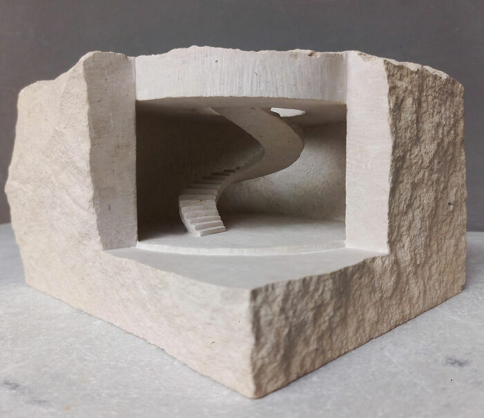 Artist carves a tiny architectural model of a spiral staircase into solid stone, showcasing intricate detail.