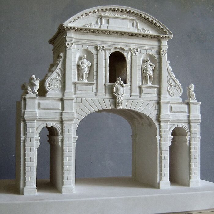 Artist carves tiny architectural models of ancient buildings into solid stone, depicting a detailed classical archway.