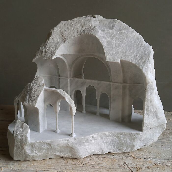 Artist carves a tiny architectural model of a classical building into solid stone, with a detailed interior.