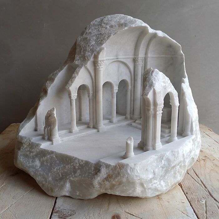 Artist carves a tiny architectural model of an ancient building into solid stone, featuring multiple arches.