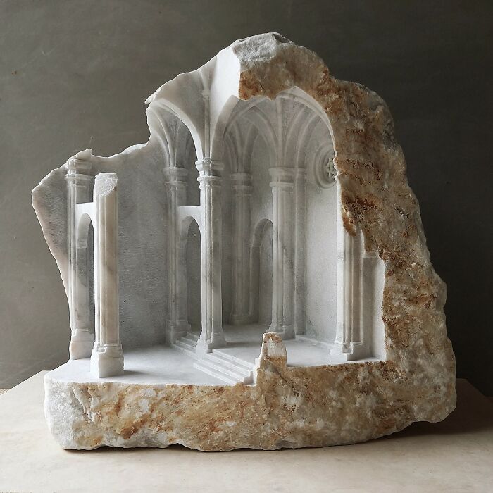 Artist carves a tiny architectural model of a classical building into solid stone, showcasing intricate details.