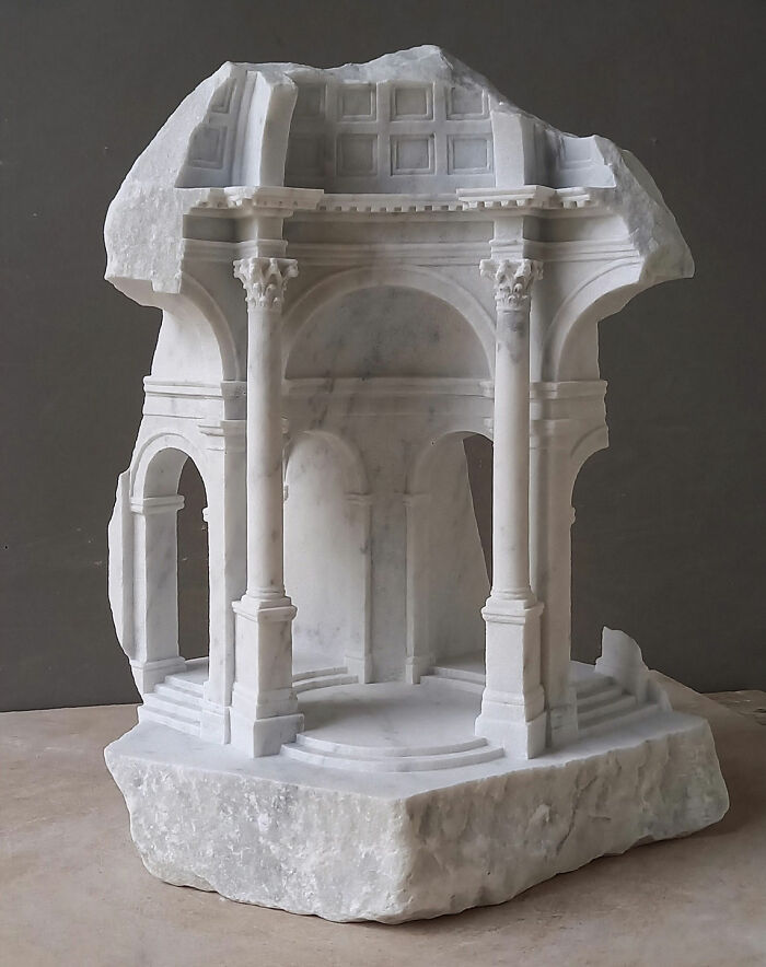 Artist carves a tiny architectural model of an ancient building into solid stone with a detailed roof.