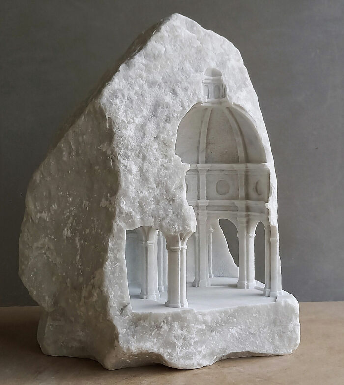 Artist carves a tiny architectural model of a classical building into solid stone, featuring a domed structure.