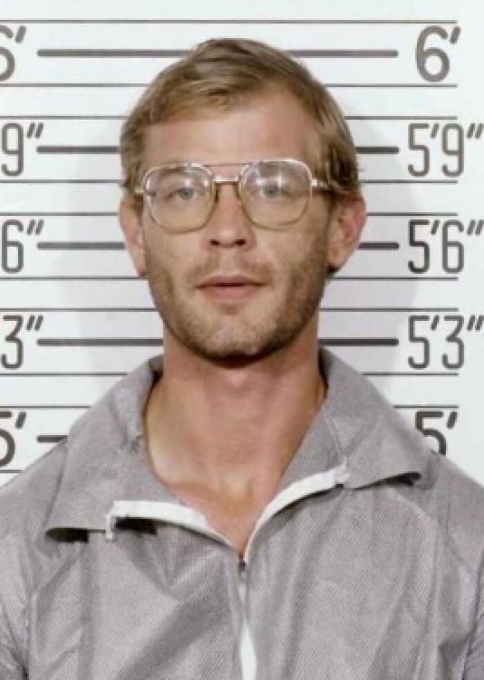 Mugshot of a man in front of height chart with glasses for disturbing serial killer facts