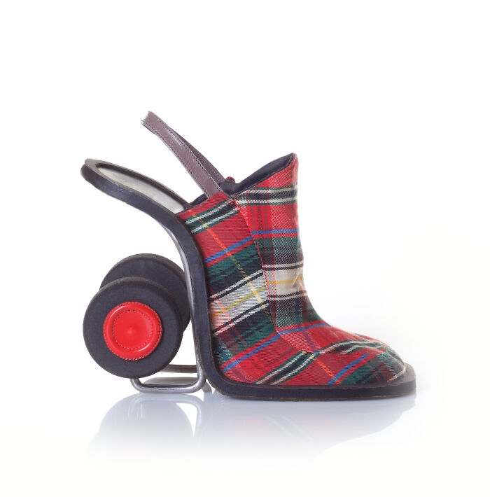 A single creative shoe by Kobi Levi in a red plaid pattern, designed with wheels like a wheeled suitcase.