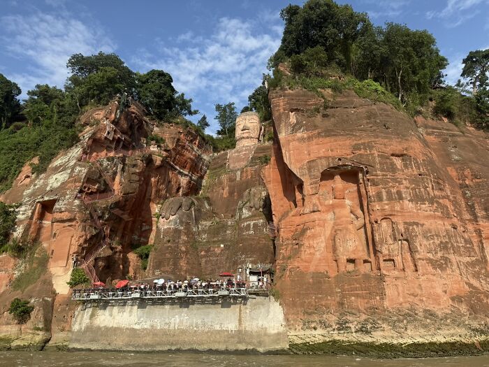 A majestic carved Buddha statue overlooking a river, showcasing the unique cultural landscape of China for a traveler.