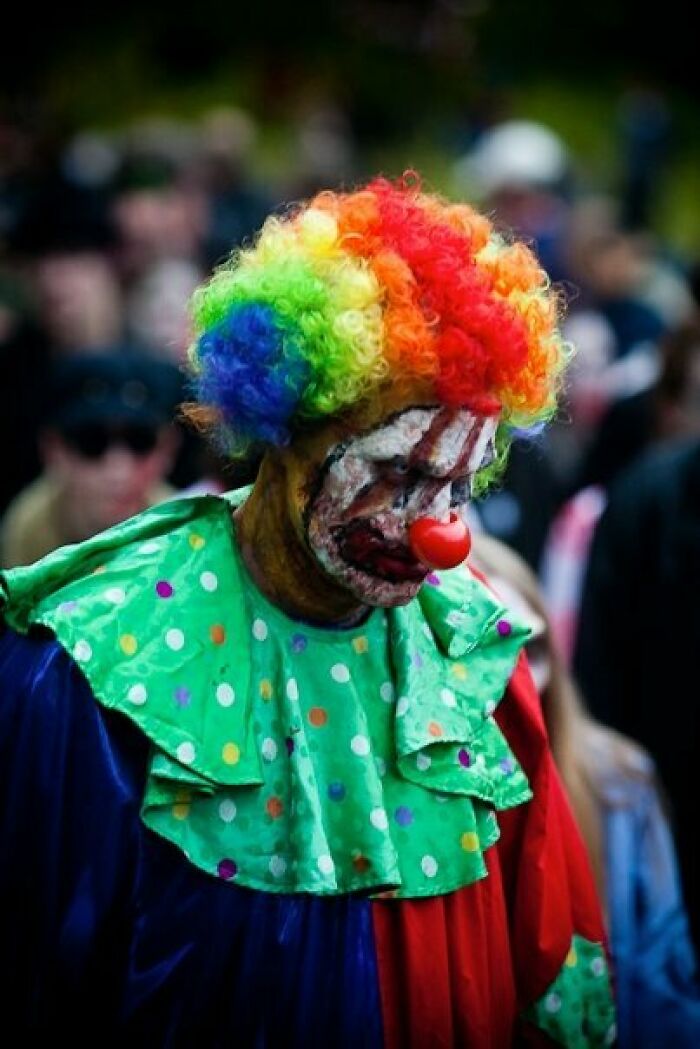 Scary clown with rainbow wig and smeared makeup at event