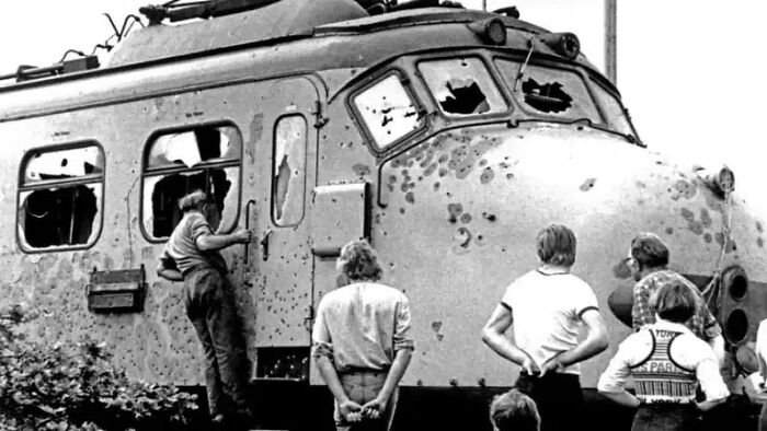 Historical photos: Several men observing a train riddled with bullet holes and shattered windows.