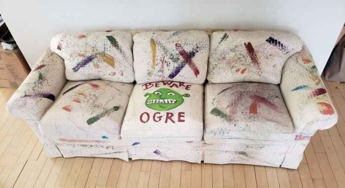 A white couch with colorful abstract paint splatters and a Shrek 'Beware Ogre' cushion, inspiring interior designer couch ideas.