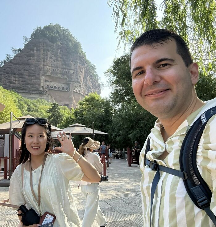 Traveler and woman smiling, exploring China, with a mountain cliff in the background.