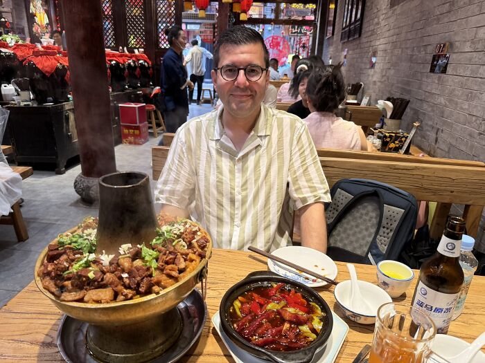 A traveler smiling at a table with a large, steaming hotpot and other dishes in a restaurant in China.