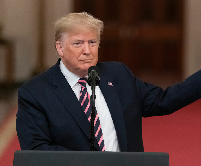 Former President Trump speaking at a podium in a suit and striped tie