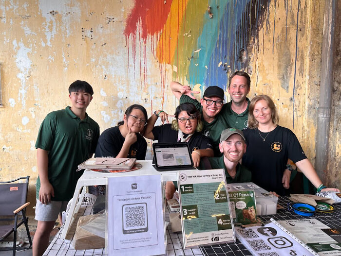 Group of volunteers smiling behind a table with information about helping street cats, showcasing local action and technology.