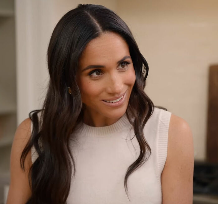 Meghan Markle smiling, with long dark hair, wearing a white sleeveless top, intensifying concern for her kids. Meghan Markle smiling, with long dark hair, wearing a white sleeveless top, intensifying concern for her kids.