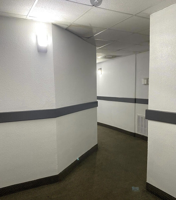 A long, deserted hallway with white walls and dark carpet, a classic example of a haunting liminal space.
