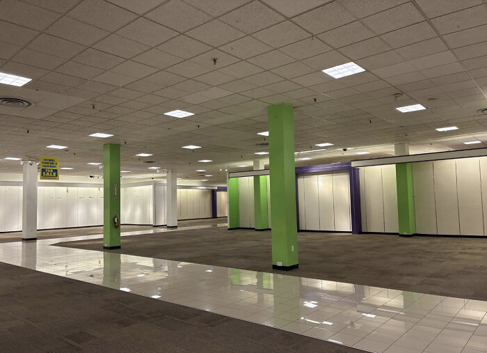 A vast, empty retail store with green pillars and bare shelves, a haunting liminal space.